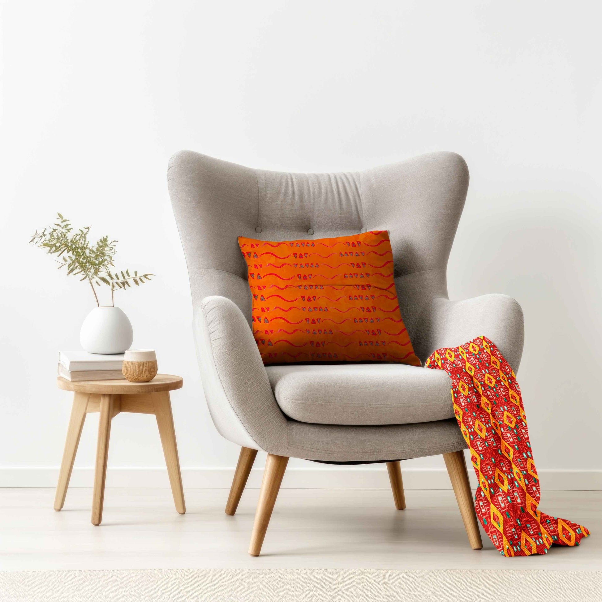 Gray armchair with an orange pillow and patterned blanket, next to a small wooden table with a plant and books.