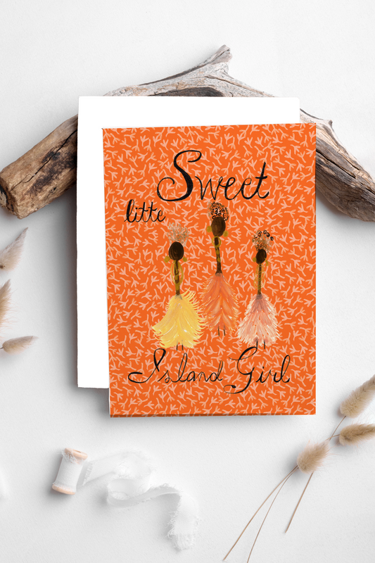 An orange greeting card with a patterned background and three illustrated girls in yellow, pink, and peach dresses, styled on a white surface with driftwood and dried grasses.